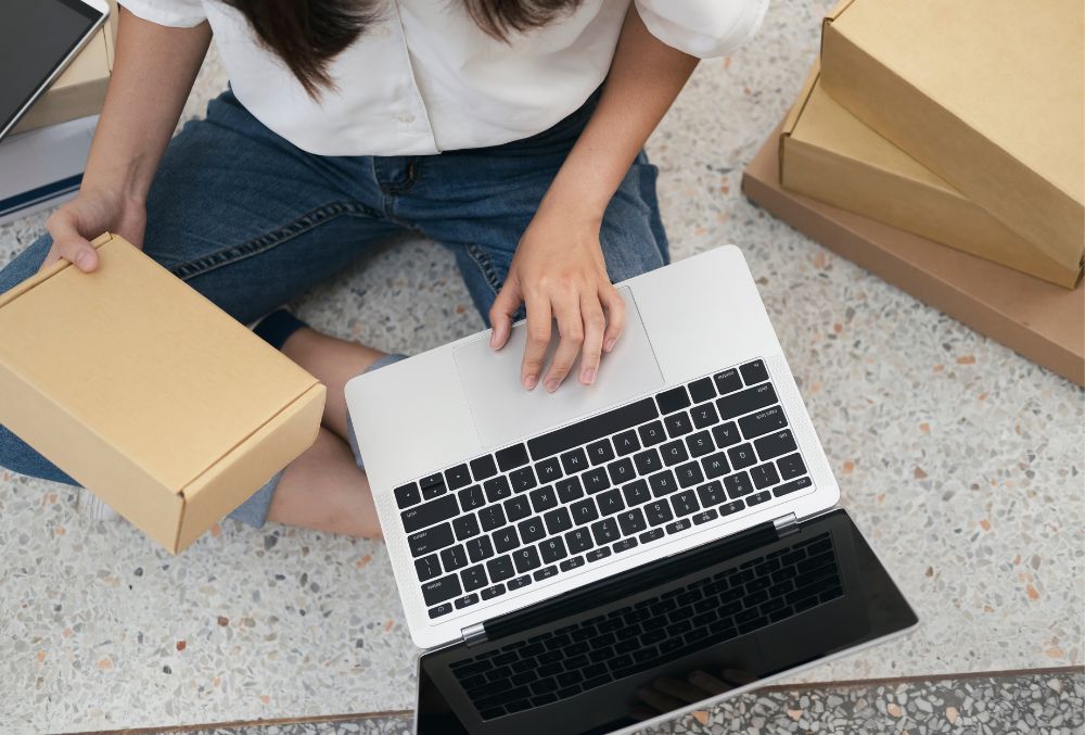 A woman holding an inventory box in one hand, and laptop in other hand.