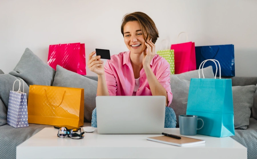 A smiling e-commerce customer with her laptop and shopping bags.