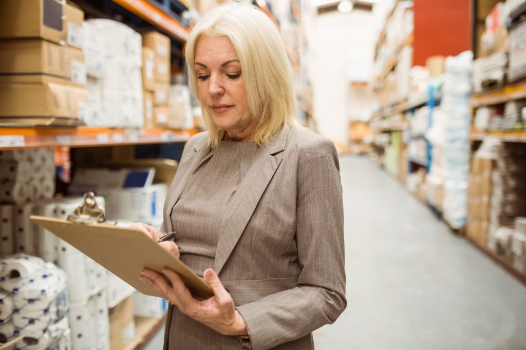 Focused female manager holding clipboard in a large warehouse